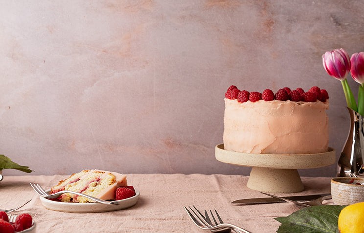 A cake with raspberries, a slice, and flowers on a table.