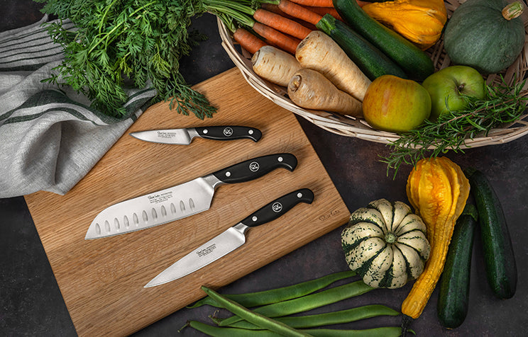 Kitchen scene with Professional knives and various vegetables on a chopping board.